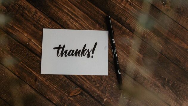 A white card with 'thanks!' written on it, placed on a dark wooden background, Next to it is a black pen.